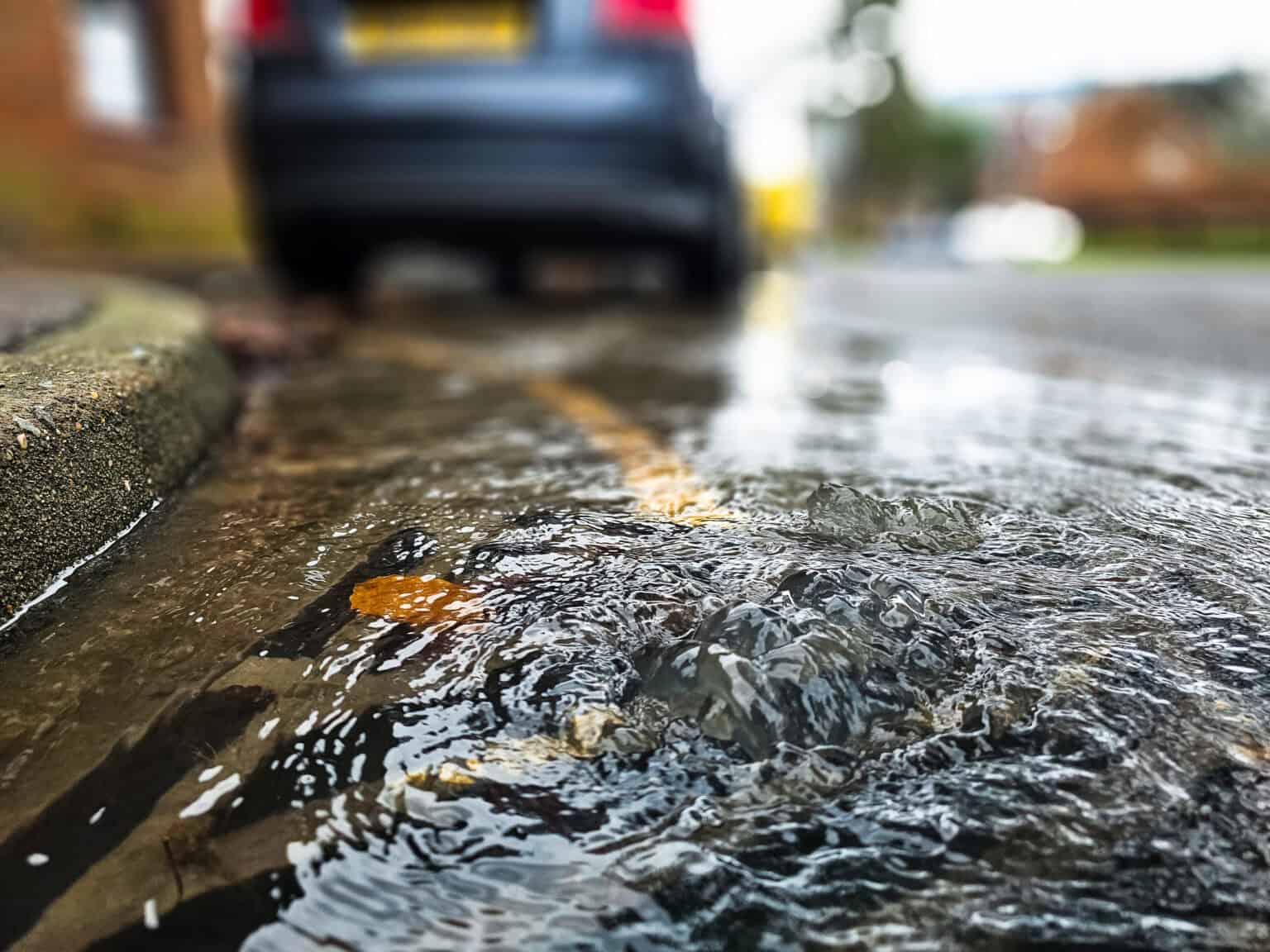 Stormwater flooding on urban street with curb and parked car.